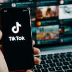 Een afbeelding van het logo van TikTok op een mobiele telefoon met op de achtergrond een reeks video's die hype vertegenwoordigen