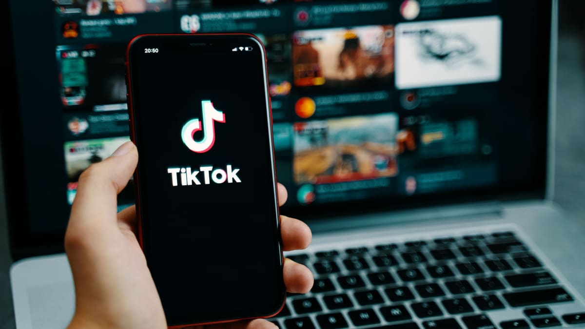 Een afbeelding van het logo van TikTok op een mobiele telefoon met op de achtergrond een reeks video's die hype vertegenwoordigen