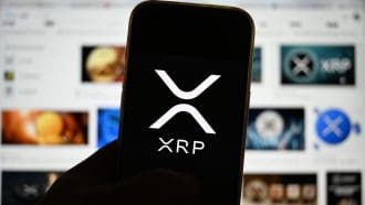 Een afbeelding van het logo van cryptomunt XRP op een mobiele telefoon met op de achtergrond veel content van de munt