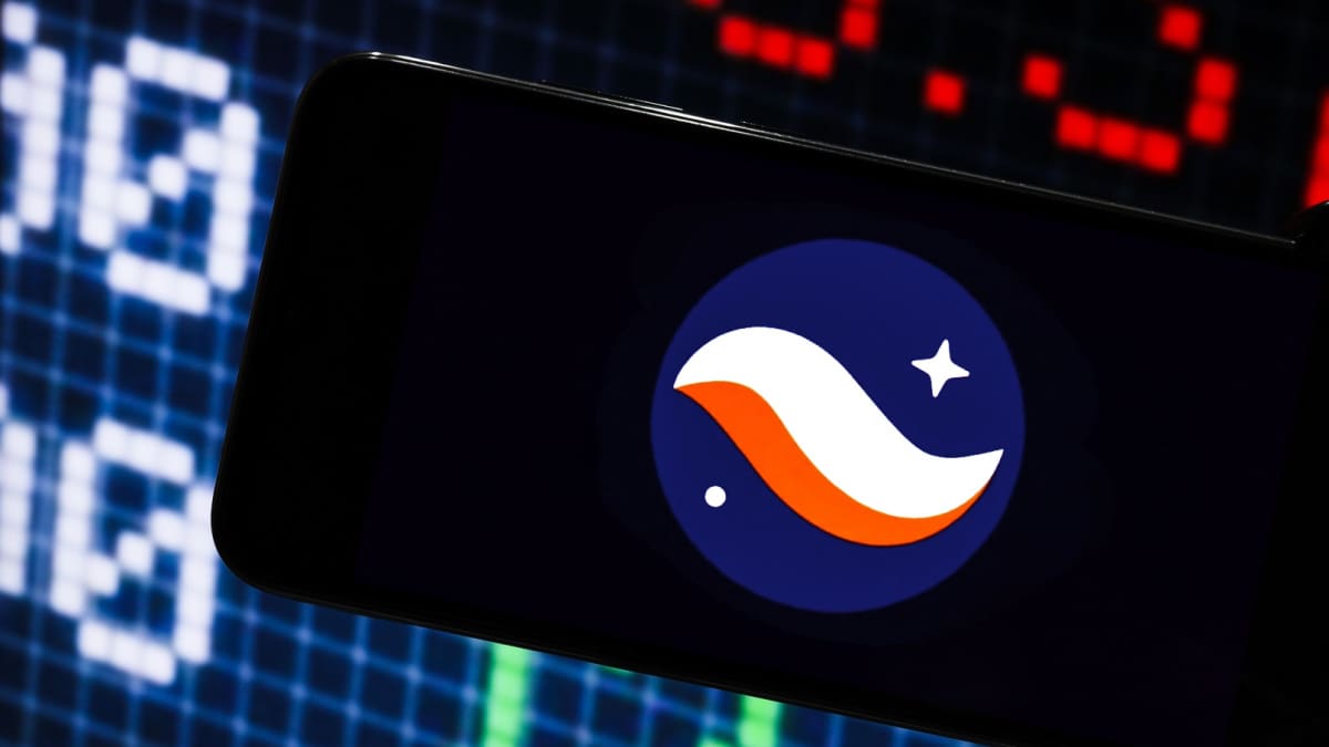 Een afbeelding van het logo van cryptomunt starknet op een mobiele telefoon met op de achtergrond marktdata en grafieken