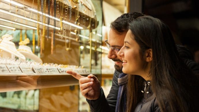 Een stel kijkt naar gouden sieraden die zijn belegd met edelstenen bij een juwelier