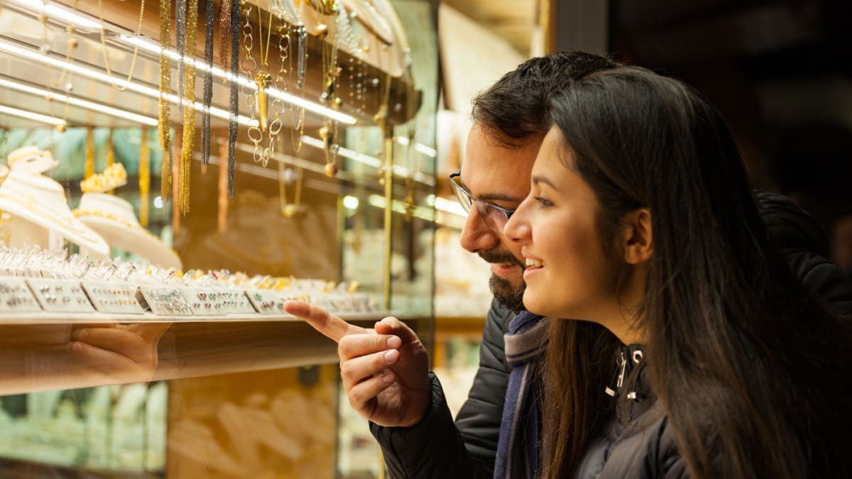 Een stel kijkt naar gouden sieraden die zijn belegd met edelstenen bij een juwelier