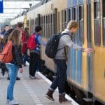 Een afbeelding van Nederlanders die op een station staan en instappen in een trein van Nederlandse Spoorwegen (NS)