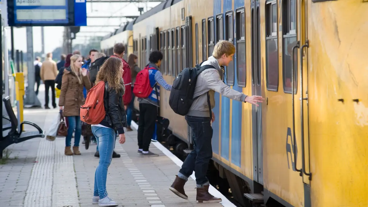 Een afbeelding van Nederlanders die op een station staan en instappen in een trein van Nederlandse Spoorwegen (NS)