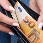 Een afbeelding van een persoon die een portemonnee opendoet om daar euro bankbiljetten uit te halen