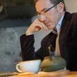 Een afbeelding van een man met een kopje koffie die thuis werkt achter zijn laptop