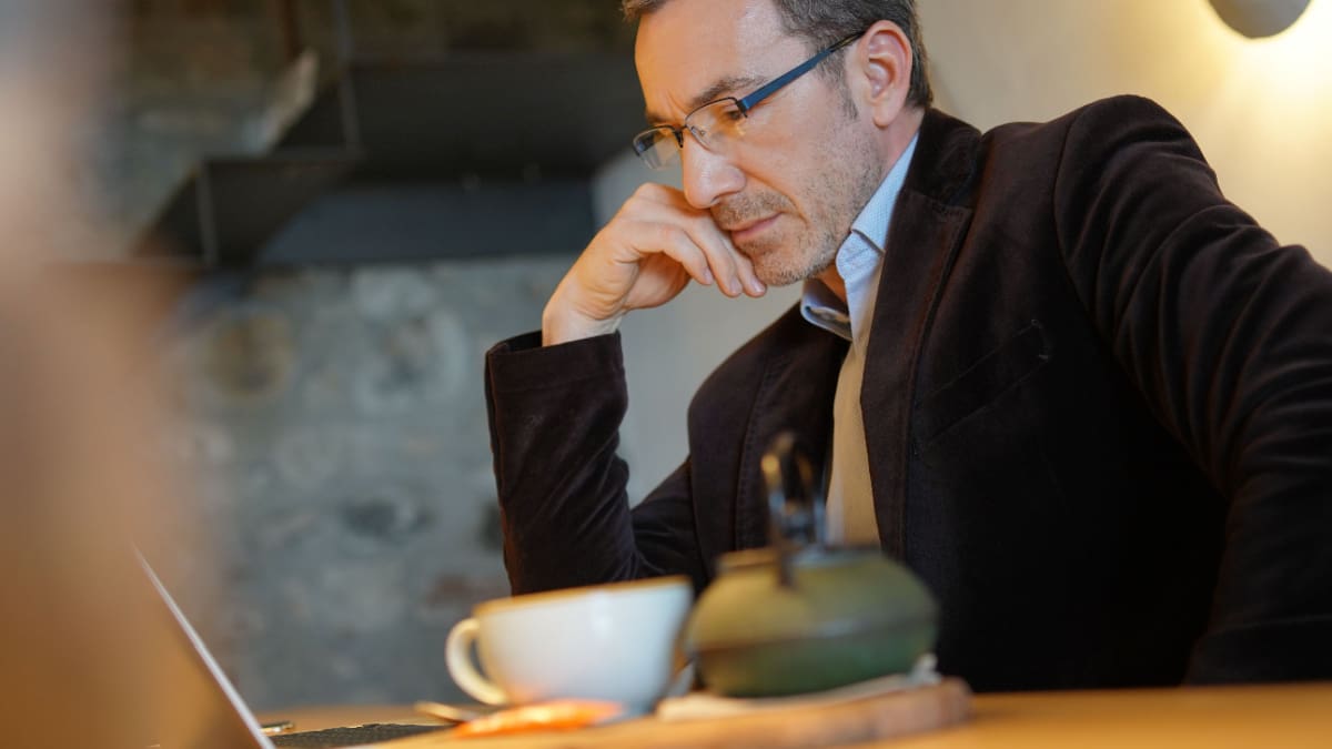 Een afbeelding van een man met een kopje koffie die thuis werkt achter zijn laptop