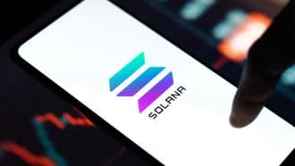 Een afbeelding van het Solana (SOL) logo op een mobiele telefoon met een koers op de achtergrond