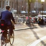 Een elegant geklede man rijdt op een fiets in het centrum van Amsterdam