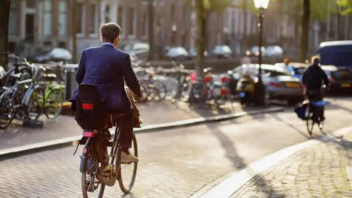 Een elegant geklede man rijdt op een fiets in het centrum van Amsterdam