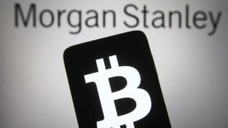 Een afbeelding van bankgigant Morgan Stanley op de achtergrond en op de voorgrond een mobiele telefoon met het bitcoin (BTC) logo