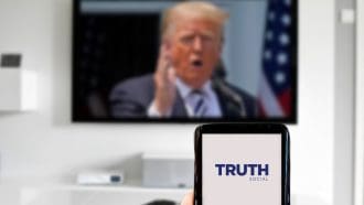 Een afbeelding van donald trump op de achtergrond met op de voorgrond een mobiele telefoon met daarop het logo van sociale mediaplatform truth social