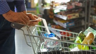 Een afbeelding van een persoon die boodschappen doet in een supermarkt met een winkelkarretje