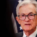 Een afbeelding van Jerome Powell met een Amerikaanse vlag op de achtergrond