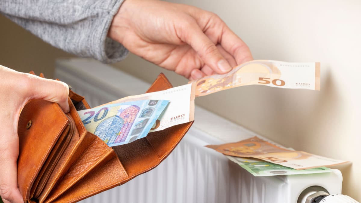 Een afbeelding van een hand die bankbiljetten uit een portemonnee haalt en op een verwarming legt