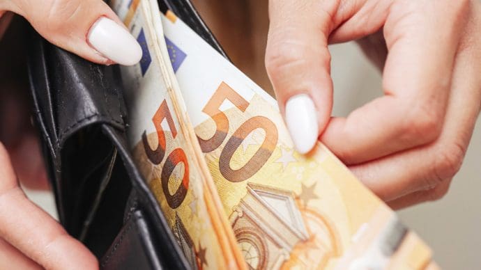 Een afbeelding van vrouwelijke handen die briefjes van 50 euro uit een portemonnee trekken