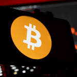 Bitcoin logo op mobiel met dalende koers in achtergrond
