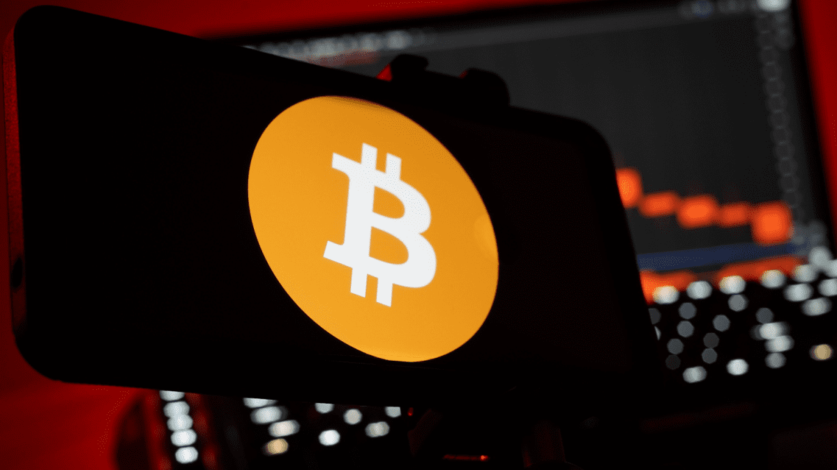Bitcoin logo op mobiel met dalende koers in achtergrond