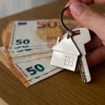 Een afbeelding van een hand die huissleutels vasthoudt voor een paar bankbiljetten van vijftig euro