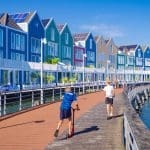 Een afbeelding van twee kinderen die spelen met een step langs het water langs een rij typisch Nederlandse huishoudens